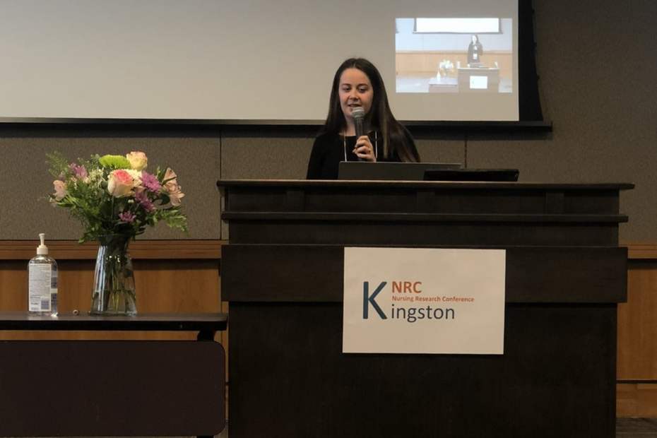 BScN student Jessica Hogan stands behind a podium presenting research findings at the Kingston Nursing Research Conference
